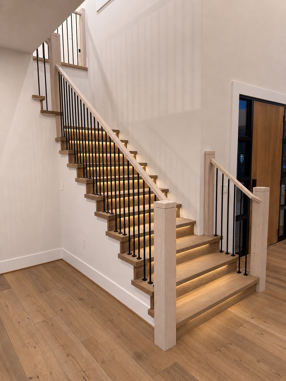 LED-lit white oak return treads and open risers with black balusters on a modern staircase in Sammamish, Washington.