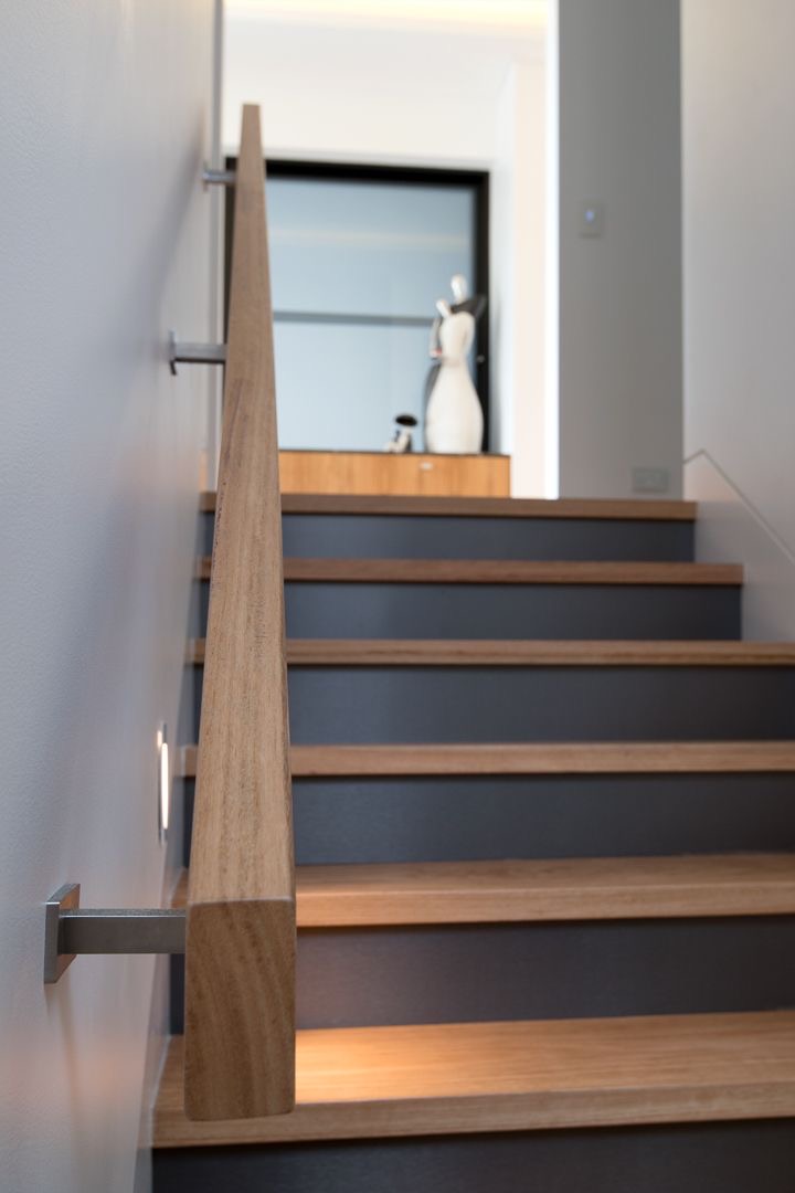 Custom tapered white oak wall-mounted handrail on stainless brackets beside oak stair treads with dark risers in Bellevue, Washington.