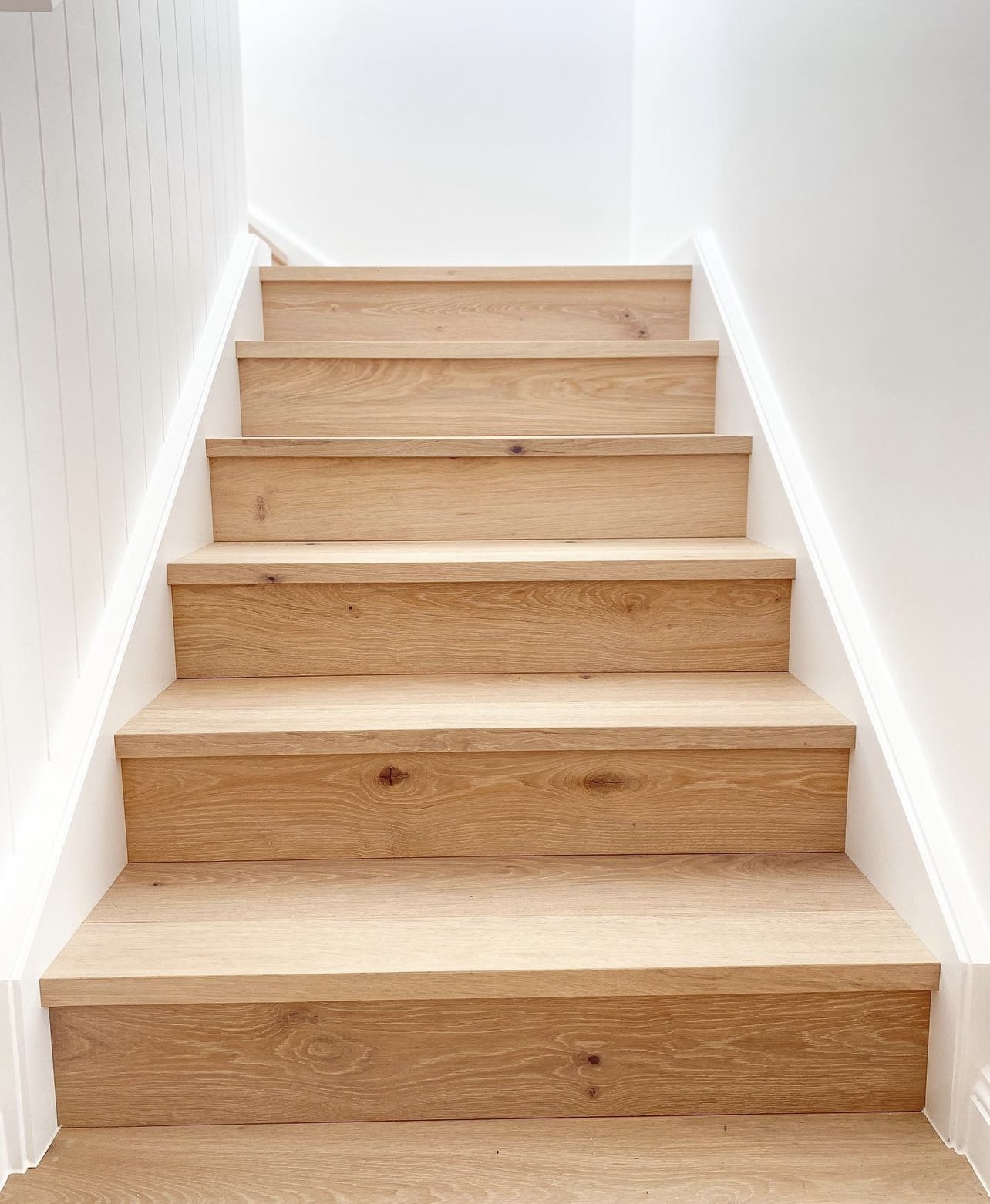 Full flight of white oak stairs with square nosings and matching risers between white walls in Renton, Washington.