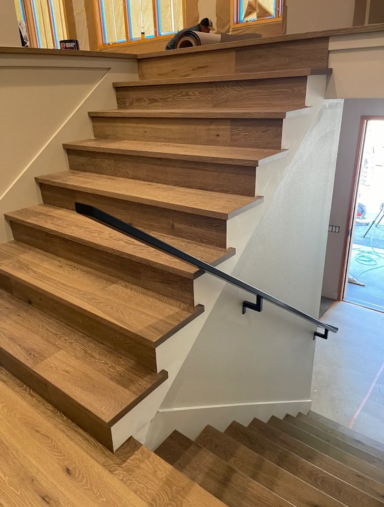 White oak return treads and matching risers on a switchback staircase with a black metal wall handrail in Seattle, Washington.