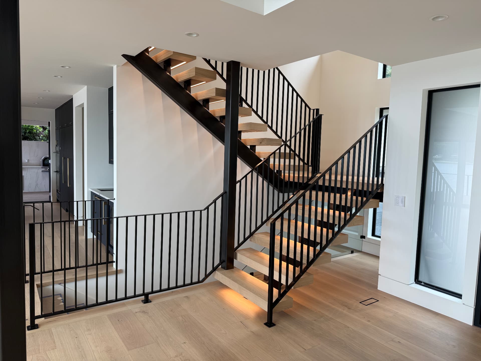 Open-riser white oak block tread staircase with LED-lit treads and black picket railing in a Bellevue, Washington entry.