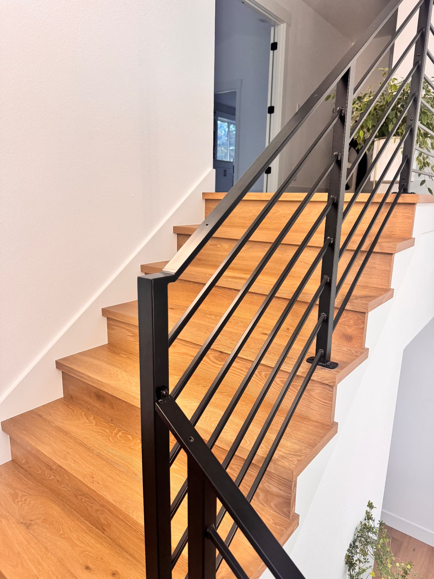 Oak return treads and risers beside a black horizontal metal railing on a straight staircase in Redmond, Washington.