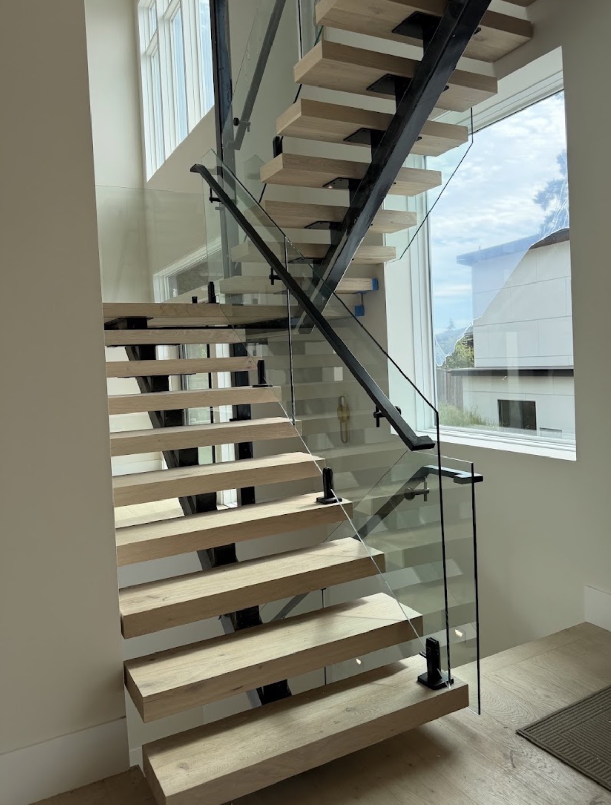 Floating white oak block tread staircase with black steel mono-stringer and frameless glass railing in a Bellevue, Washington home.