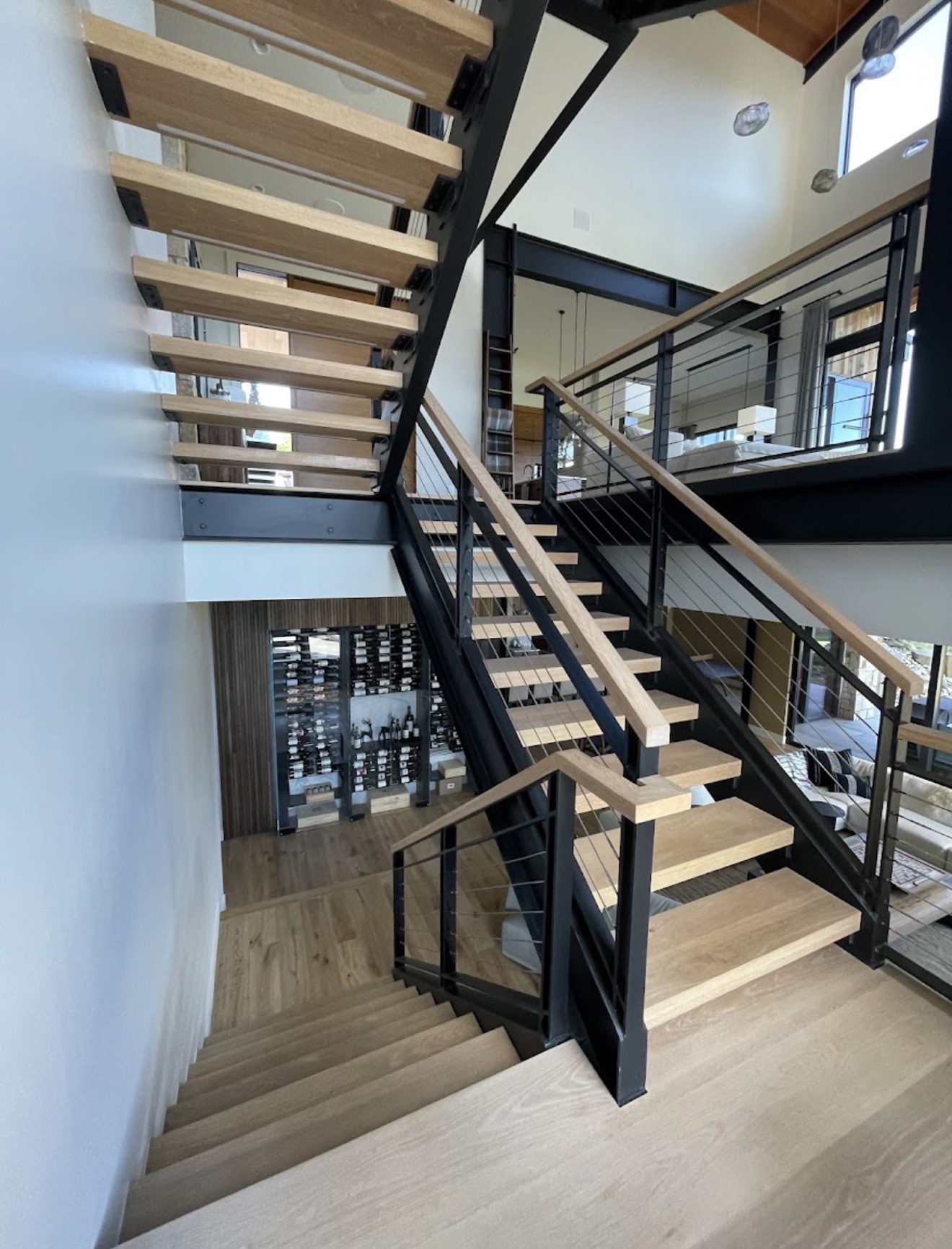 Open-riser white oak block tread staircase with black steel stringers, white oak handrail and horizontal cable railing in a Seattle, Washington home.