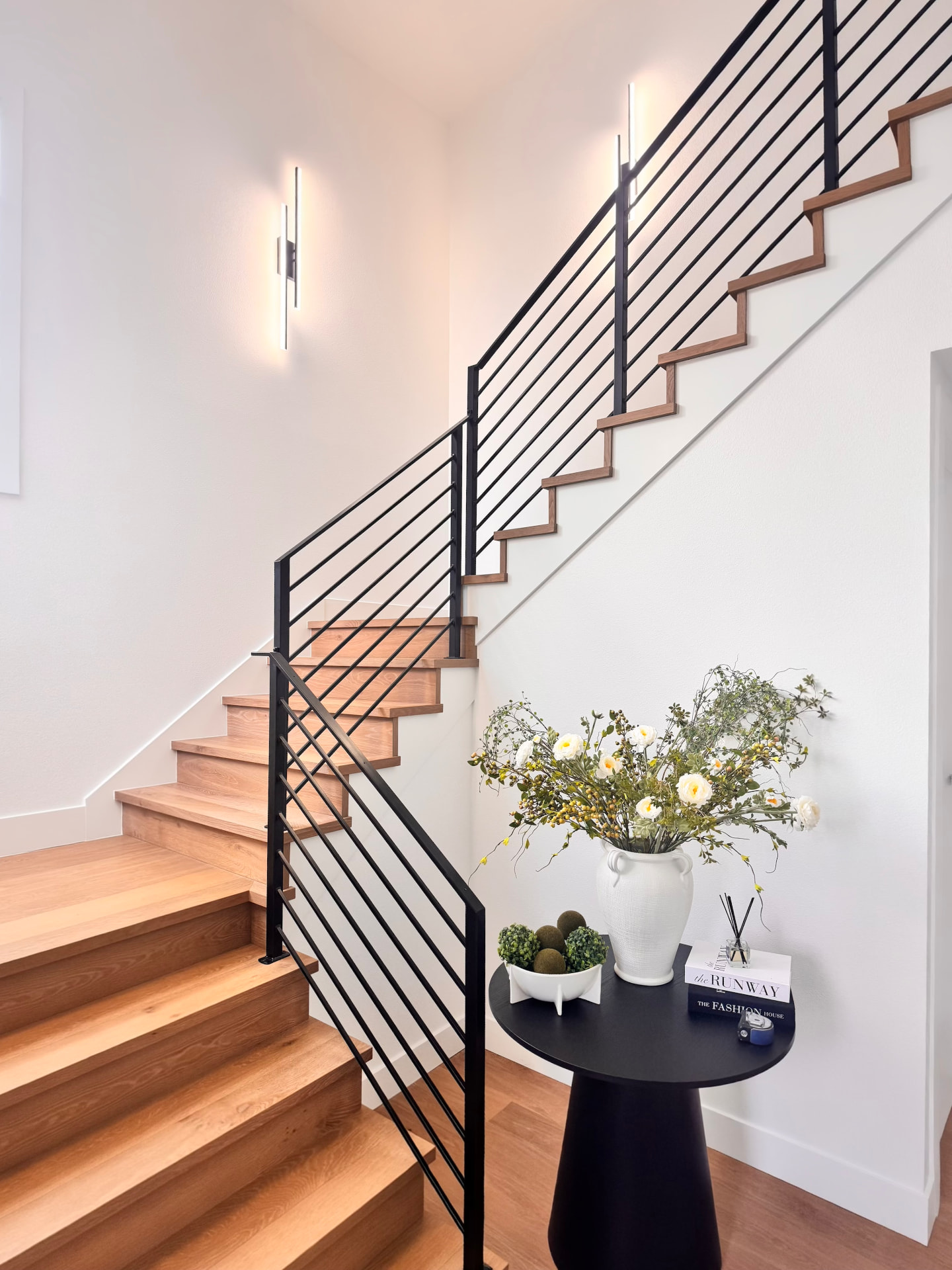 White oak return treads and risers on an L-shaped staircase with a black horizontal bar railing and linear wall sconces in Seattle, Washington.