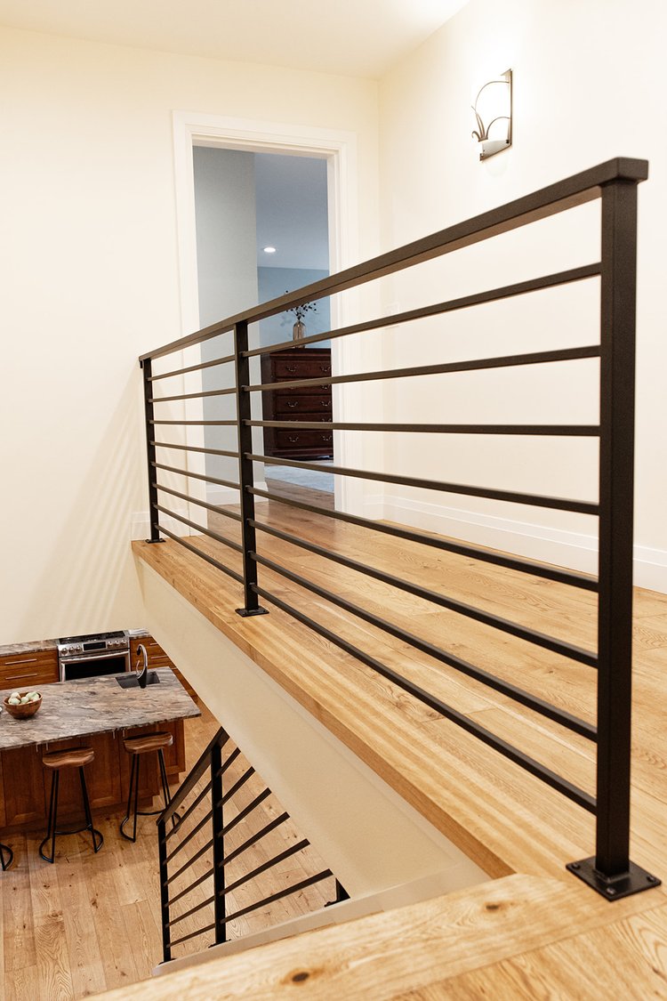 White oak wallcap and landing treads with a horizontal black metal railing overlooking a kitchen in Bellevue, Washington.
