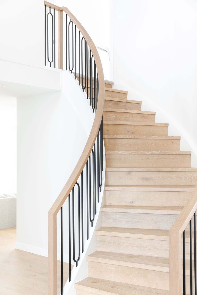 Curved staircase with light white oak treads, risers and a wood-capped handrail with black balusters in Kirkland, Washington.